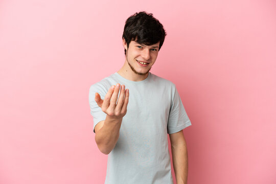 Young Russian man isolated on pink background inviting to come with hand. Happy that you came