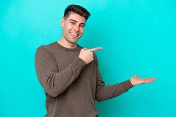 Fototapeta premium Young caucasian man isolated on blue background holding copyspace imaginary on the palm to insert an ad