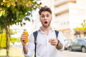 Fototapeta premium Young handsome man holding an orange juice at outdoors surprised and pointing front