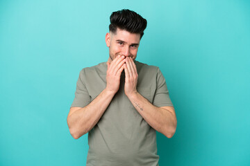 Young caucasian man isolated on blue background happy and smiling covering mouth with hands
