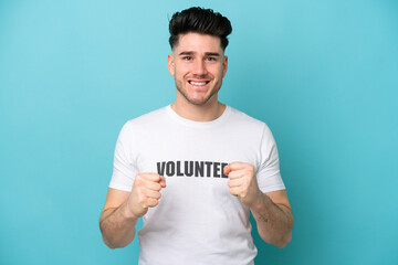 Young volunteer caucasian man isolated on blue background celebrating a victory in winner position