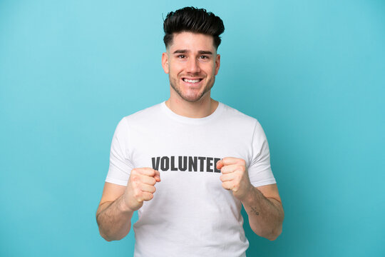 Young volunteer caucasian man isolated on blue background celebrating a victory in winner position