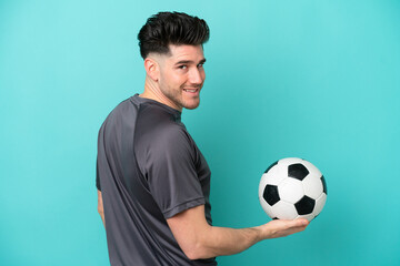 Young caucasian man isolated on blue background with soccer ball