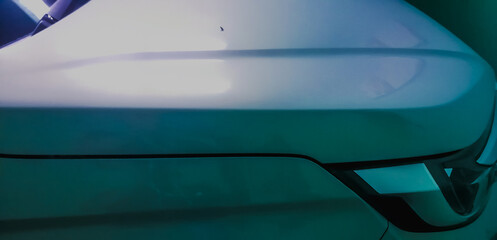 Detail of the side view of a modern car hood and headlights, in a parking space