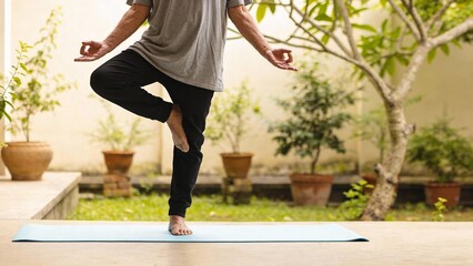 Man practicing yoga in outdoor setting with green plants around  