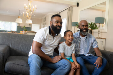 Fototapeta premium African American three-generation family sitting on gray sofa with chandelier near kitchen island