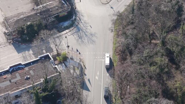 Aerial view of rural road intersection near small buildings, trees, and fields, captured by drone in early spring daylight.