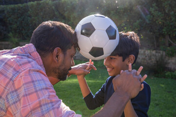 Indian father with son pressing soccer ball between foreheads while balancing wrists in backyard © wavebreak3