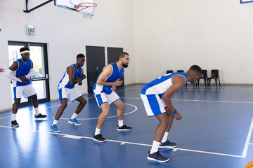 Fototapeta premium Diverse male teammates guarding in low stance on gym court with basketball hoop