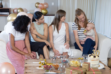 Obraz premium Diverse female friends celebrating turning thirty with baby in living room with cake, balloons