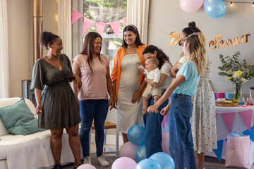 Obraz premium Diverse family with friends standing around pregnant woman in living room with baby shower banner