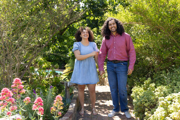 Fototapeta premium Couple strolling hand in hand along brick pathway in garden with flower beds, green shrubs