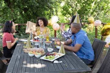 Obraz premium Diverse friends celebrating on deck around table opening gift bag beside charcuterie board