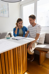 Obraz premium Couple in casual clothing reviewing papers on clipboard at kitchen nook with mug on white tabletop