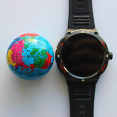 A modern digital clock with mode buttons on the bezel near a small classic globe on a white table. A symbolic photo on the theme of modern and past times
