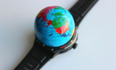 A black smartwatch with a silicone strap under a miniature globe. A symbolic stem photo on the theme of world time