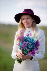 Woman holding a colorful bouquet while wearing a stylish hat in a peaceful outdoor setting during daylight