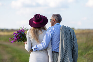 Couple enjoying a sunny day while walking along a country path with flowers and casual attire in a scenic landscape