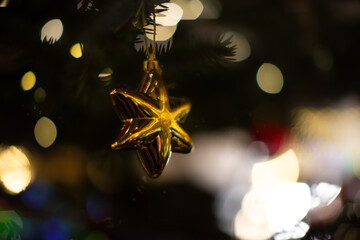 Shining gold star ornament hanging on a Christmas tree with colorful lights in the background during the holiday season