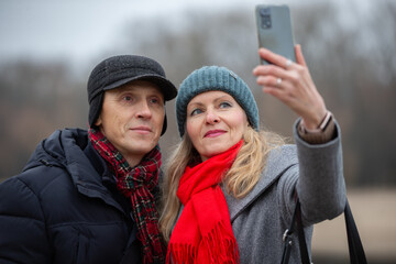 Couple taking a selfie outdoors while enjoying a cool day with warm clothing in a park setting
