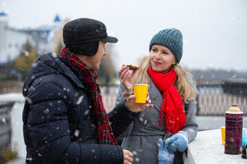 Couple enjoying snacks and drinks in snowy park during winter