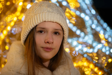 Girl in a cozy winter hat enjoying festive lights during a chilly evening in a winter market