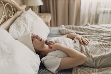 Young woman with headache flu ill sick disease cold at home indoor lying on bed with cold compress on her head at bedroom home