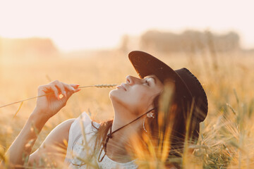Woman farmer in cowboy hat profile portrait with spikelet at agricultural field on sunset. © primipil