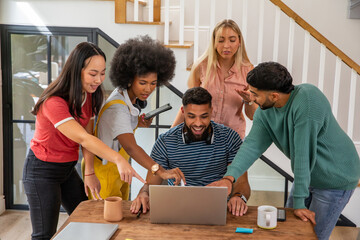 Diverse student friends collaborating around laptop at staircase base with tablet, headphones © wavebreak3