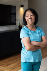 Asian senior woman standing in living room with console, flat-screen TV, potted orchid, wall sconce