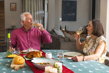 Senior couple sitting at dining table in living room with roasted chicken centerpiece and wine