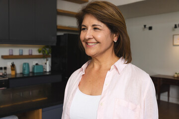 Hispanic middle-aged woman smiling and looking off in kitchen near teal toaster, kettle, copy space
