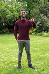 African american man standing on mown lawn at park pointing forward near flowerbed in sweater
