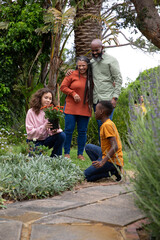Diverse family kneeling and standing in lush backyard garden holding potted plant