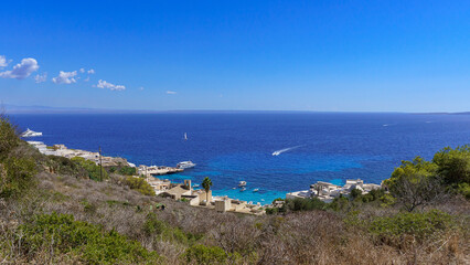 A stunning aerial view of the picturesque fishing village and harbor of Levanzo Island, Sicily, showcasing its white Mediterranean architecture nestled against the vibrant deep blue of the sea.