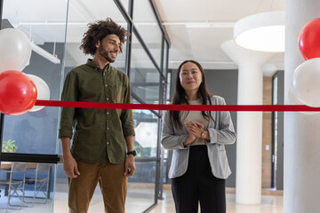 Diverse coworkers in business attire standing behind ribbon in reception area with balloons