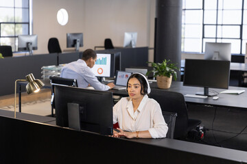 Diverse female coworkers working on computer monitors and headsets in office