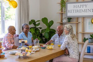 Obraz premium Diverse senior friends celebrating retirement at home dining table with cupcake stand, banner