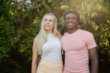 Obraz premium Diverse couple standing in sunlit garden in white top, light skirt and pale pink shirt