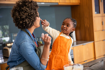 African american mother and daughter mixing batter in kitchen, daughter in orange apron