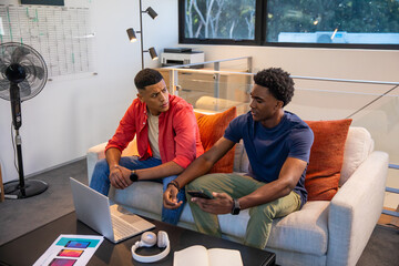 Diverse male colleagues discussing design concepts over laptop and phone mockups in office lounge