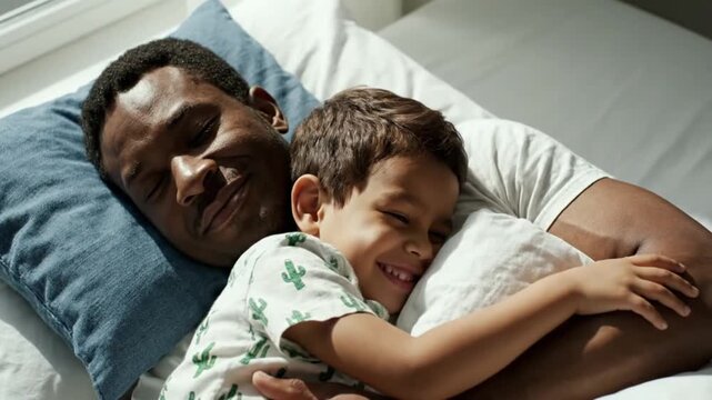 Affectionate African American Father and Son Cuddling and Laughing Together in Bed During a Happy Morning Bonding Moment at Home