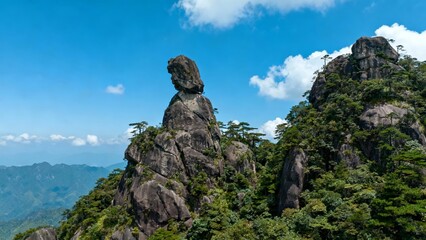 A striking rock formation balanced atop a mountain peak amidst lush greenery under a clear blue sky