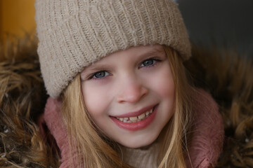 Fototapeta premium Outdoor winter portrait of adorable 8 year old girl wearing woolen hat and pink jacket