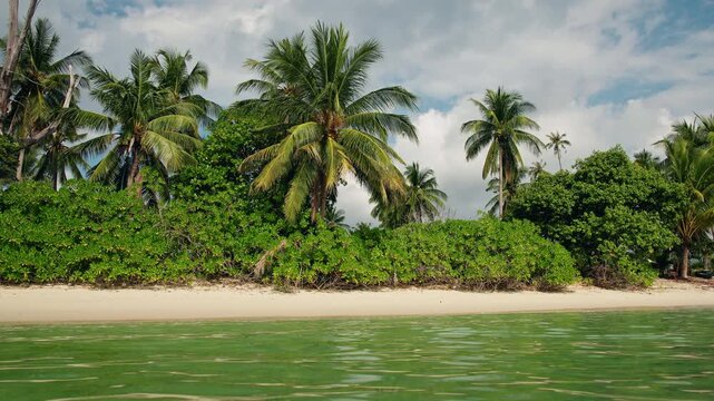 Tropical beach with coconut palms and lush green vegetation along sandy shoreline at Lipa Noi on Koh Samui under cloudy sky and calm shallow sea