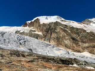 An impressive mountain glacier near Saas Fee in Valais, Switzerland, surrounded by imposing Swiss mountain peaks under a clear blue sky. Massive ice formations and rugged alpine terrain, Swiss Alps