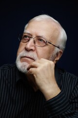 Obraz premium Elderly man with glasses and white beard thinking about life in a dark room