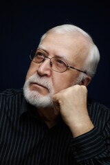 Fototapeta premium Senior man with glasses resting chin on hand and looking thoughtfully into distance indoors