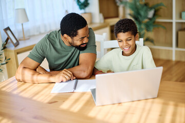Fototapeta na wymiar Father and son doing homework with laptop at home. Father and teenage son using laptop. Boy and dad sitting at home working with notebook