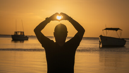 silhouette of man on the beach forming heart with his hands catching the sunset